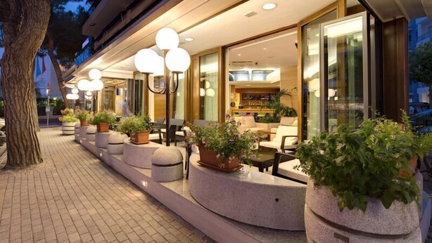 A hotel exterior with outdoor seating, potted plants, and a well-lit entrance. - Astromare (Jesolo)
