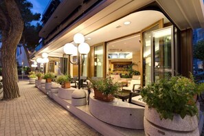 L’extérieur d’un hôtel, avec une terrasse, des plantes en pot et une entrée bien éclairée.