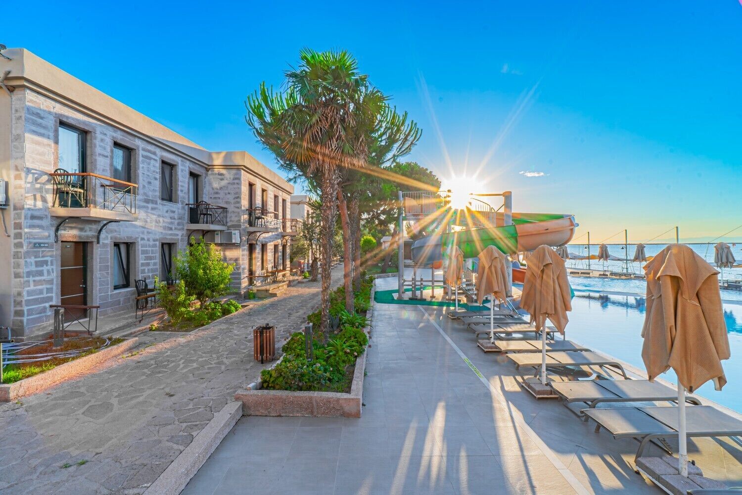 Een kusthotel met stenen gebouwen, terras en een zwembadgedeelte met parasols.