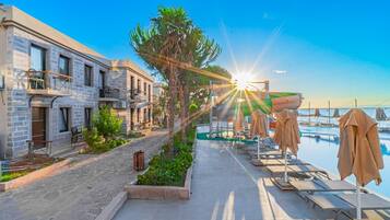 Een kusthotel met stenen gebouwen, terras en een zwembadgedeelte met parasols.
