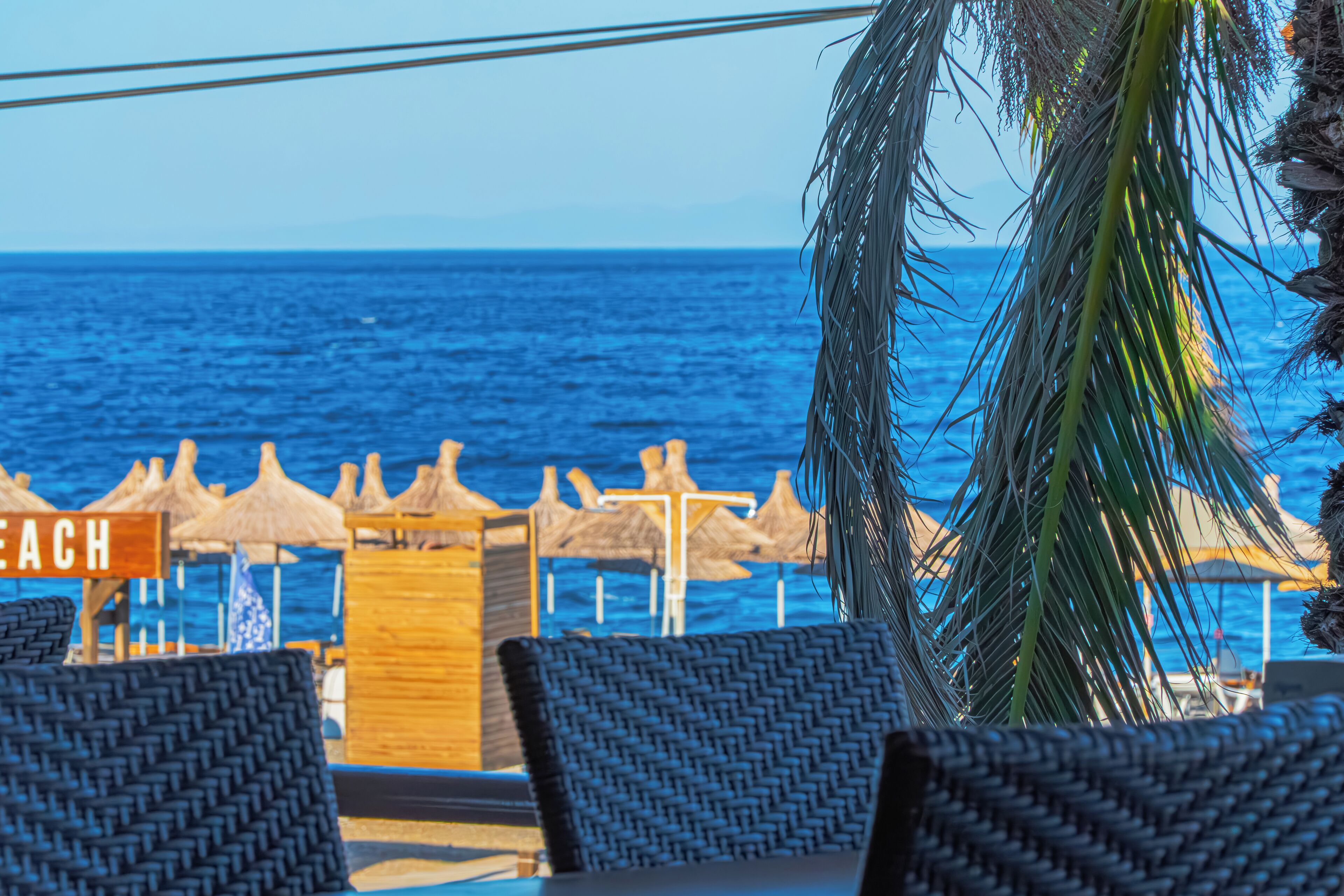 A beachside seating area with wicker chairs and thatched umbrellas, overlooking the ocean.