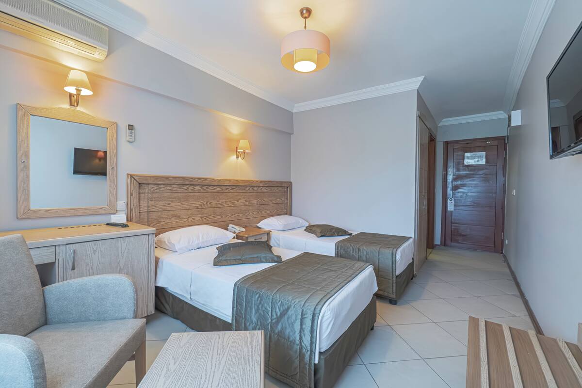 A hotel room with a bed, bedside tables, a chair, a desk, a mirror, and a television.