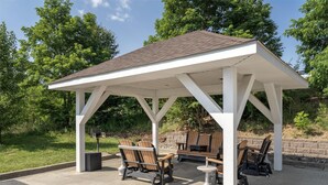 A covered outdoor seating area with wooden chairs and tables, surrounded by greenery. - SureStay Plus Hotel by Best Western Keyser (Keyser)