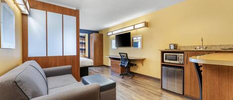 Une chambre d’hôtel compacte comprenant un canapé, un bureau, une télévision, un four à micro-ondes et une petite kitchenette.