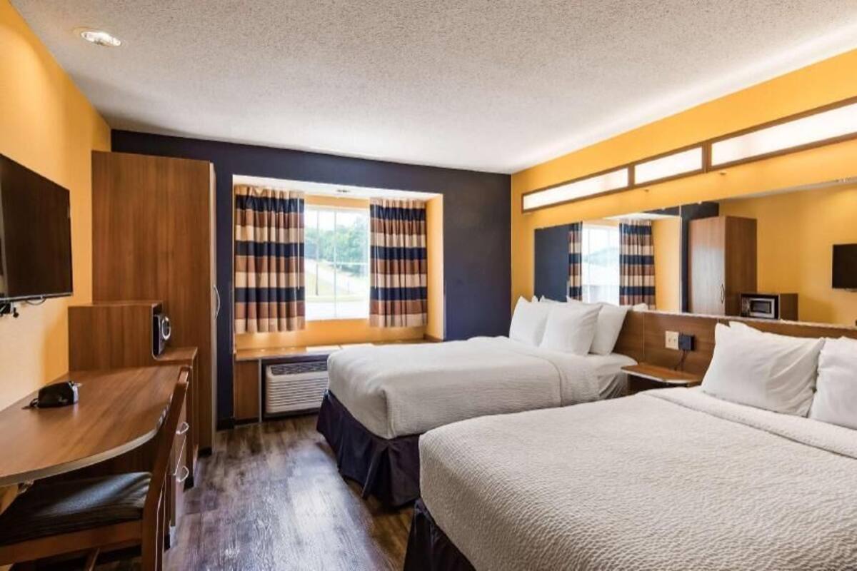 A hotel room with two beds, a desk, a TV, and a window with curtains.
