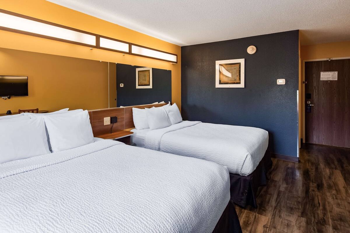 A hotel room with two beds, a TV, a desk, and a door.