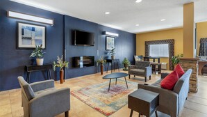 A modern living room with a sofa, armchairs, a coffee table, and a TV. There are potted plants and a fireplace. - SureStay Plus Hotel by Best Western Keyser (Keyser)