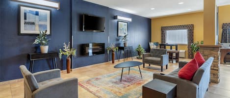 Un salon moderne avec un canapé, des fauteuils, une table basse et un téléviseur. On y trouve également des plantes en pot et une cheminée.