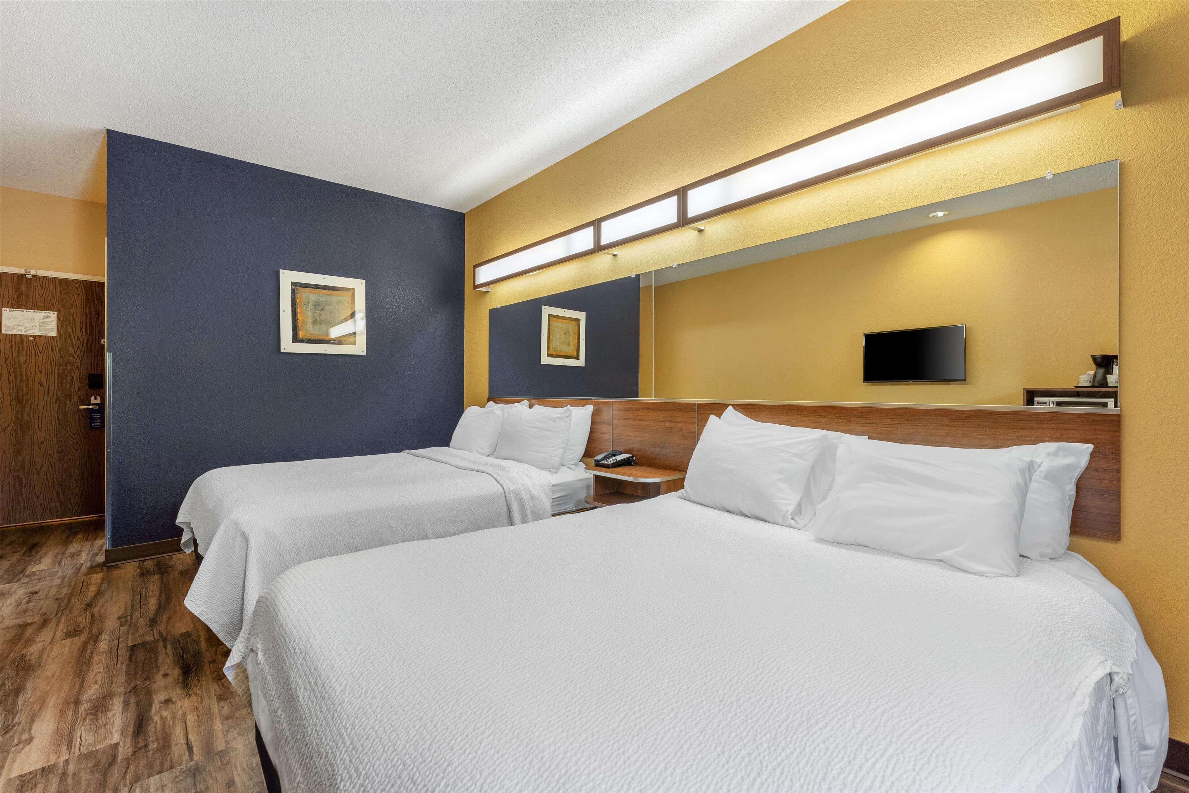 Una habitación de hotel con dos camas, un televisor de pantalla plana, una mesita de noche y un espejo.