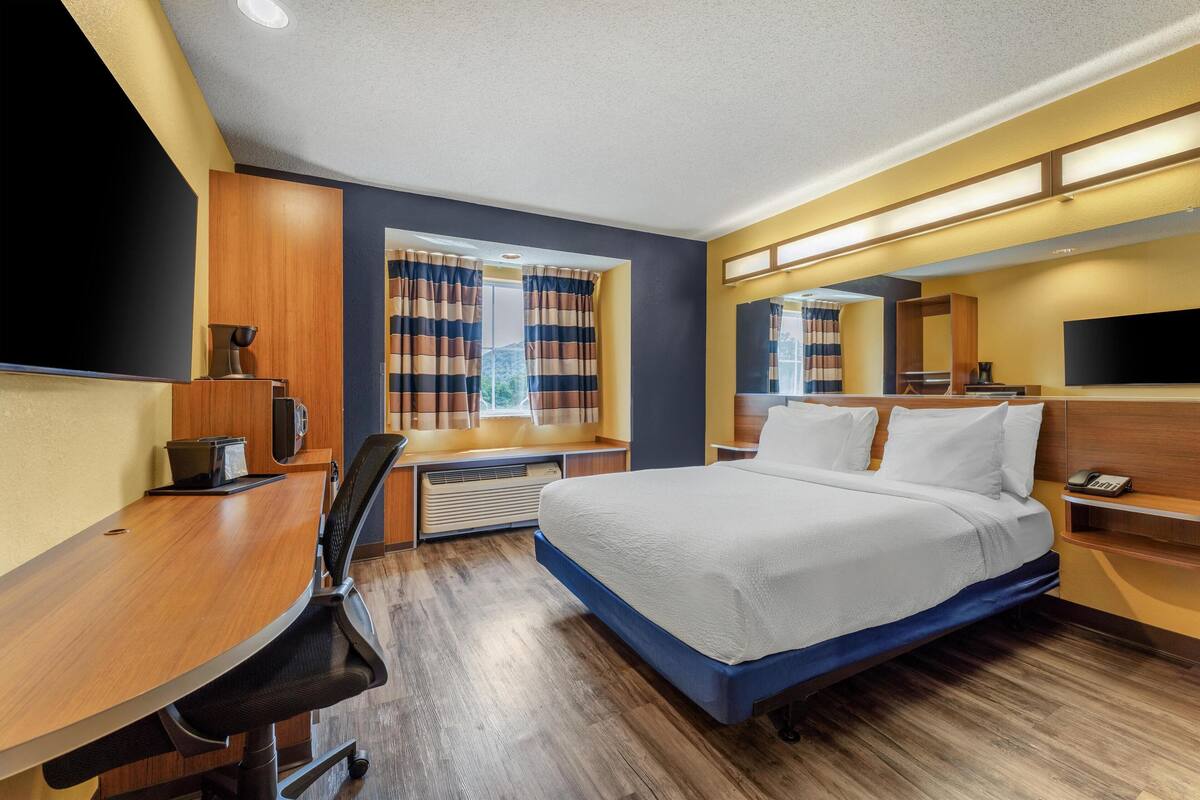A hotel room with a bed, a desk, a chair, a TV, and a window with curtains.