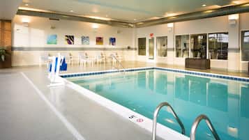 A swimming pool with clear blue water, a tiled deck, and a reception area with chairs and artwork on the wall.