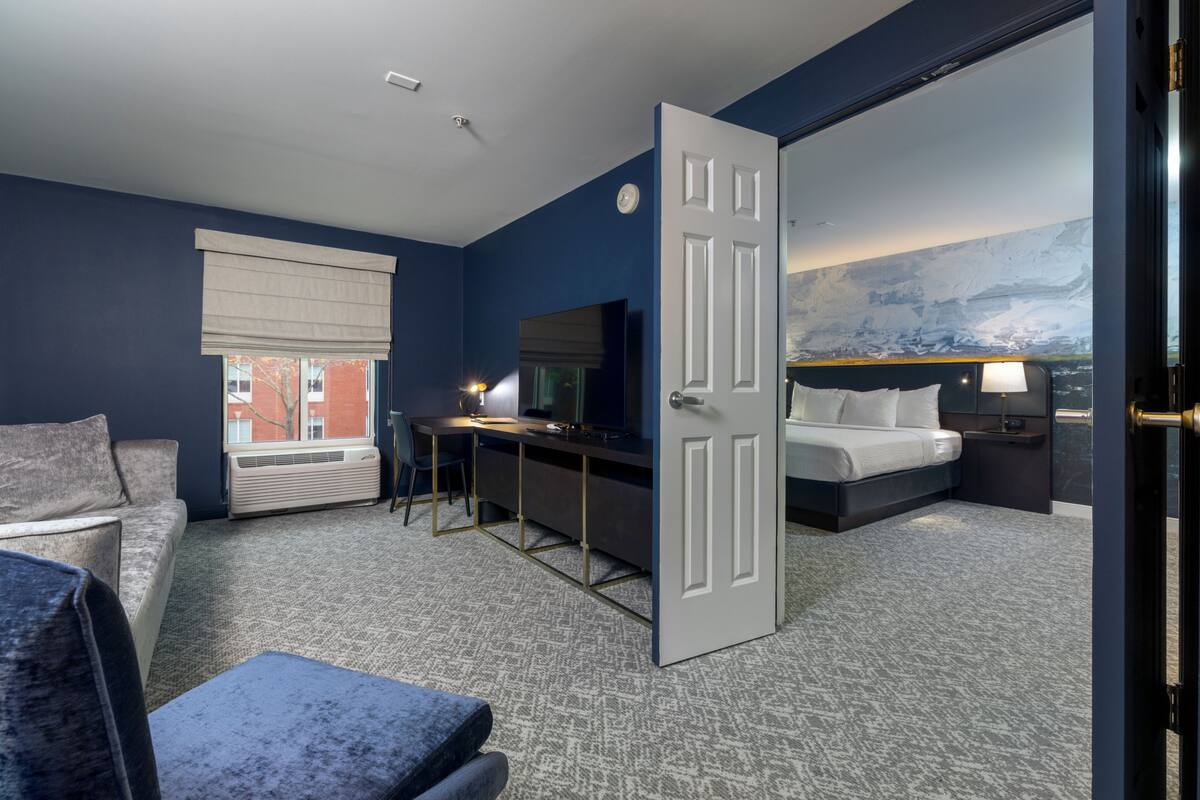 A hotel room with a bed, a desk, a chair, a couch, and a large window.