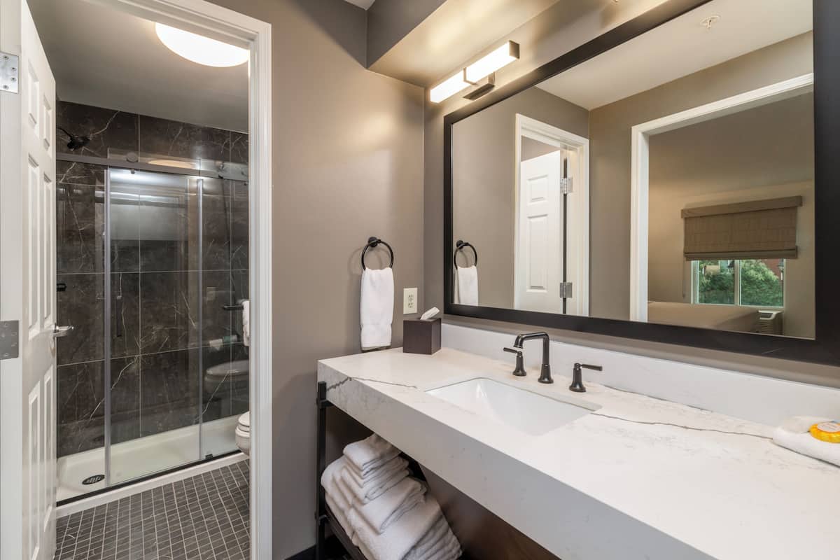 A modern bathroom with a glass-enclosed shower, a large mirror, and a white vanity with a sink.