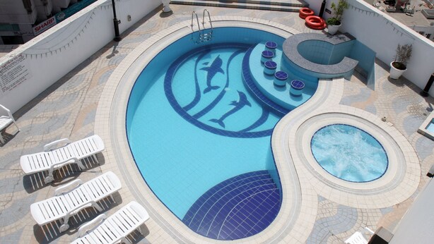 Une grande piscine extérieure avec plusieurs espaces aménagés pour se détendre et un jacuzzi.