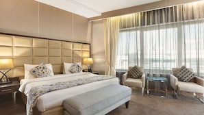 Une chambre d’hôtel avec un grand lit, deux fauteuils, une petite table ronde et une grande fenêtre avec des rideaux.