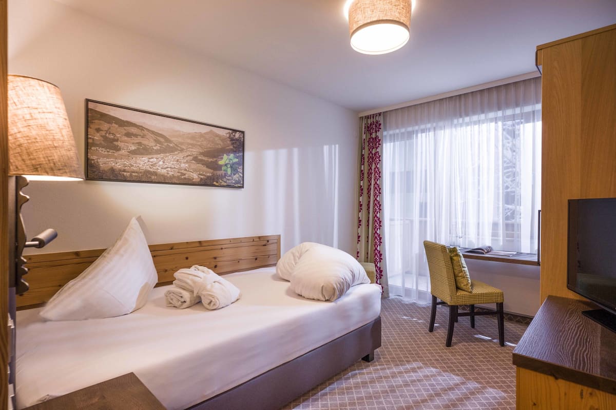 Une chambre d’hôtel avec un lit, une chaise, une télévision et une fenêtre avec des rideaux.