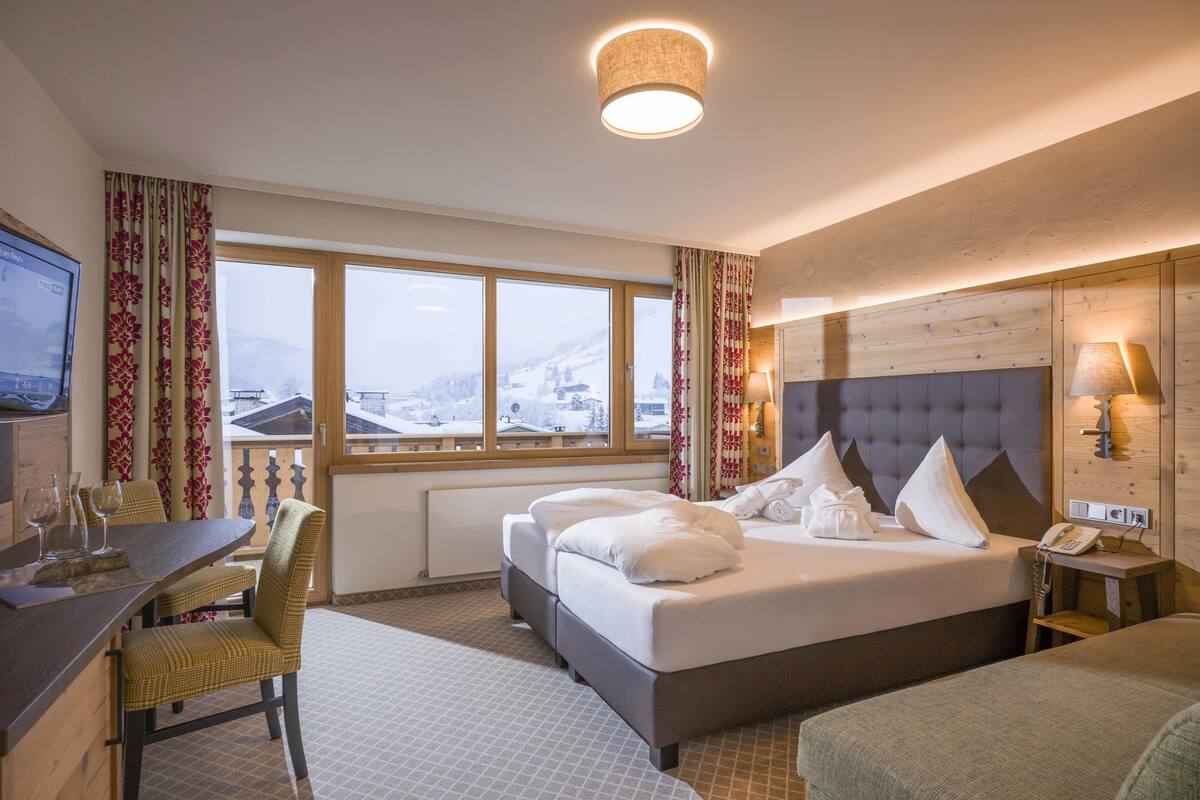 Une chambre d’hôtel avec un lit, un bureau et une chaise. Il y a une fenêtre donnant sur un paysage enneigé.
