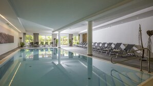 Une grande piscine intérieure dotée de chaises longues et offrant une vue sur la verdure environnante.