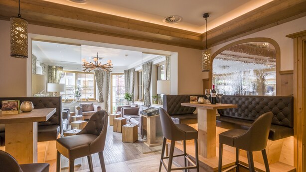 Un hall d’hôtel moderne doté d’un bar, de différents espaces de détente et offrant une vue sur l’extérieur grâce à une grande fenêtre en arc de cercle.