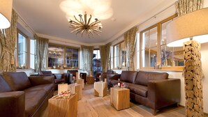 Un salon spacieux avec deux canapés en cuir marron, des tables basses en bois et un grand lustre.