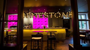 Zona de bar con letrero de neón, taburetes y mostrador con botellas.