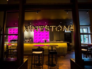 A bar area with a neon sign, bar stools, and a counter with bottles. - Mercure Ostrava Center Hotel (Ostrava)