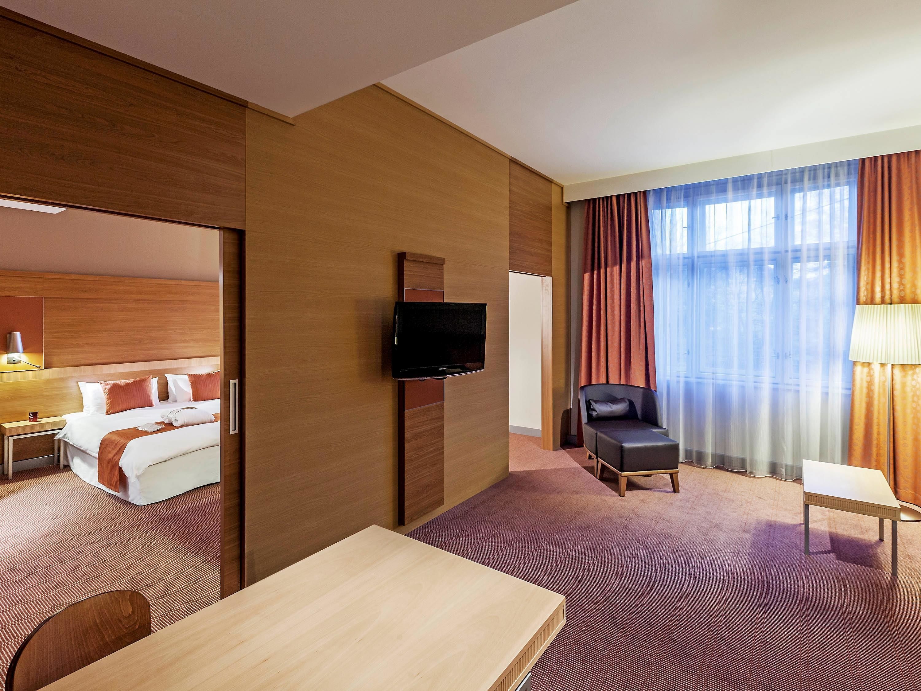Une chambre d’hôtel avec un lit, un téléviseur fixé au mur, une chaise, une petite table et une fenêtre avec des rideaux.
