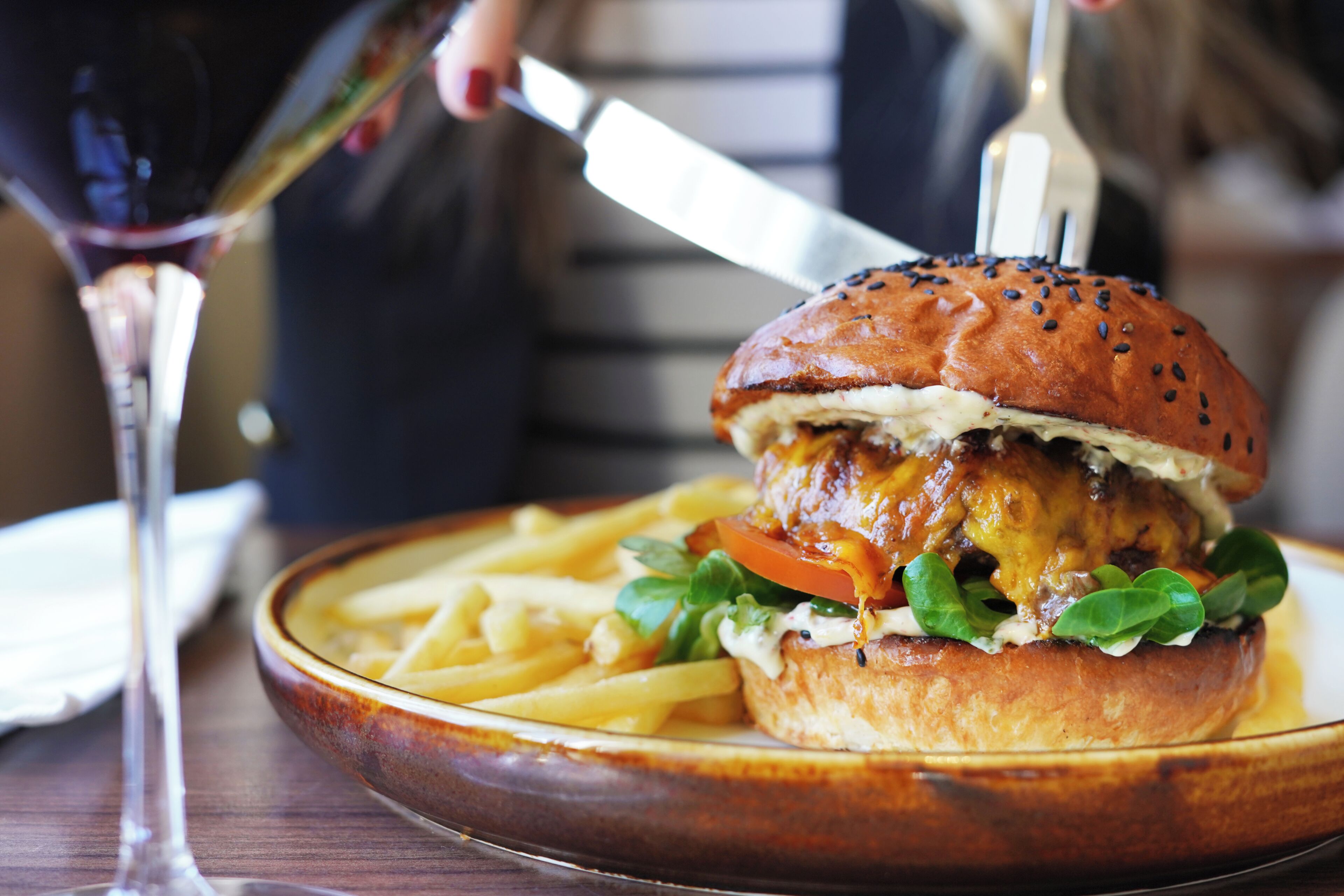A burger with fries on a plate, a glass of wine, and a fork.