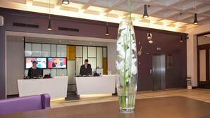 Un mostrador de recepción con una pantalla de televisión, un jarrón con flores blancas y una mesa de madera.