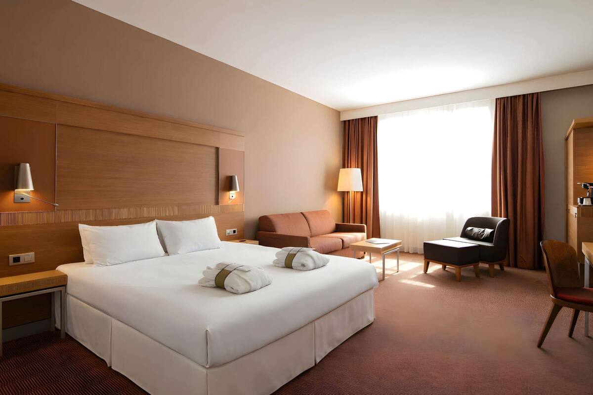 A hotel room with a large bed, a desk, a chair, and a sofa.