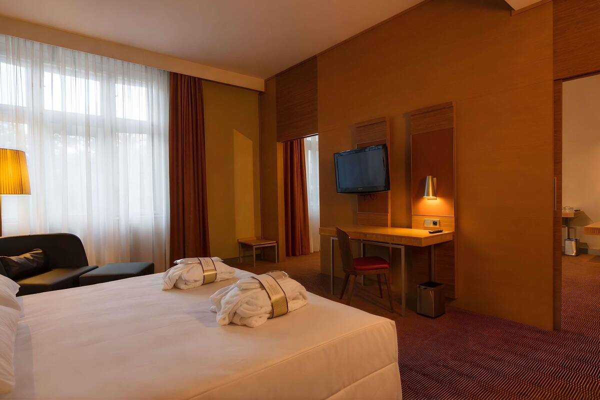 A hotel room with a bed, a desk, a chair, a TV, and a lamp.
