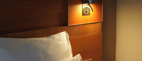 A hotel room with a wooden headboard, a bedside lamp, and a nightstand with a lamp.