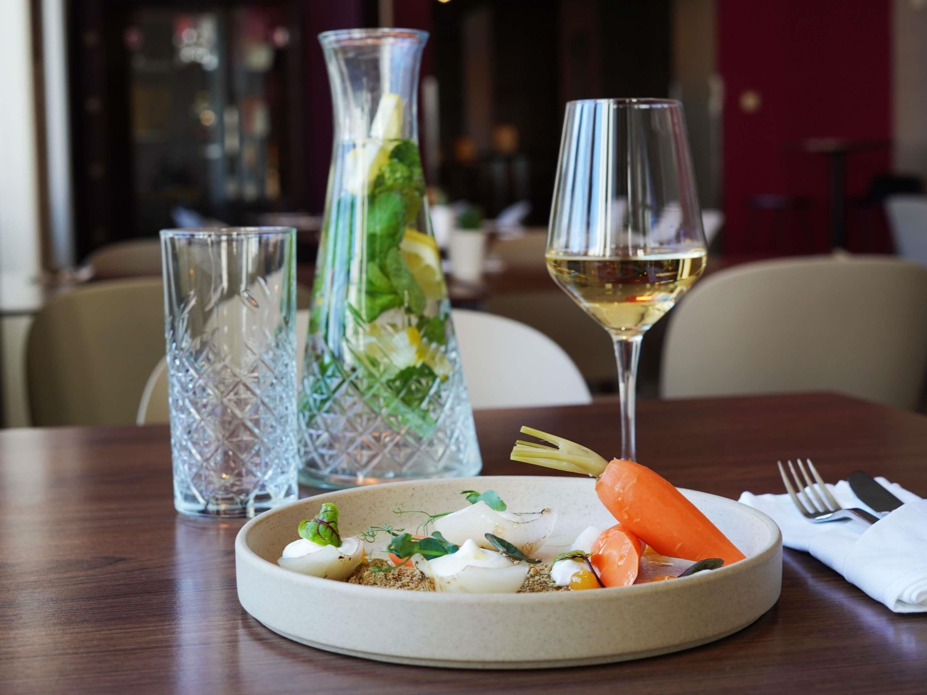 A dining table with a plate of food, a glass of white wine, and two crystal glasses.