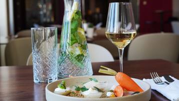A dining table with a plate of food, a glass of white wine, and two crystal glasses.