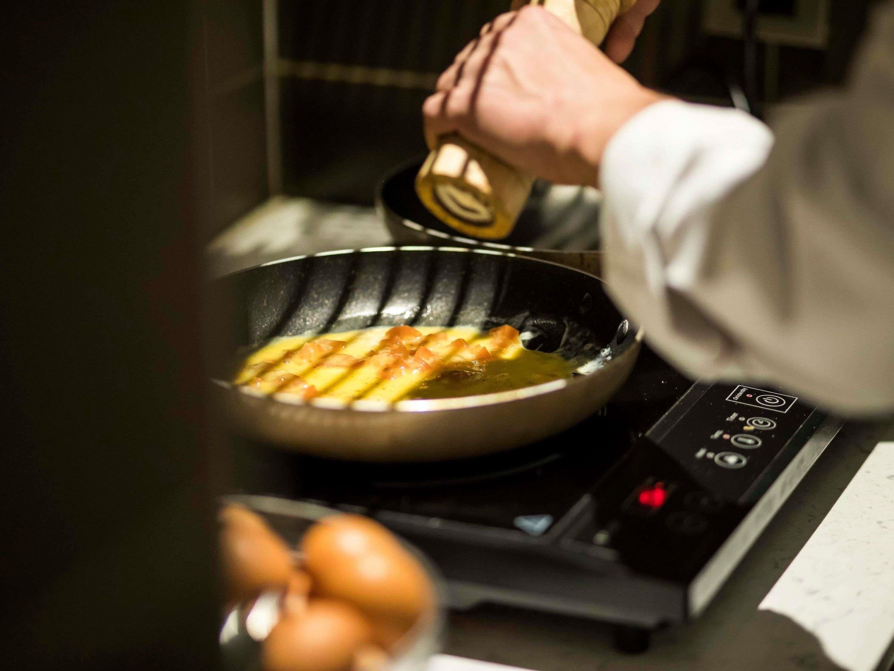 A person cooking in a kitchen with a frying pan on an induction cooktop.