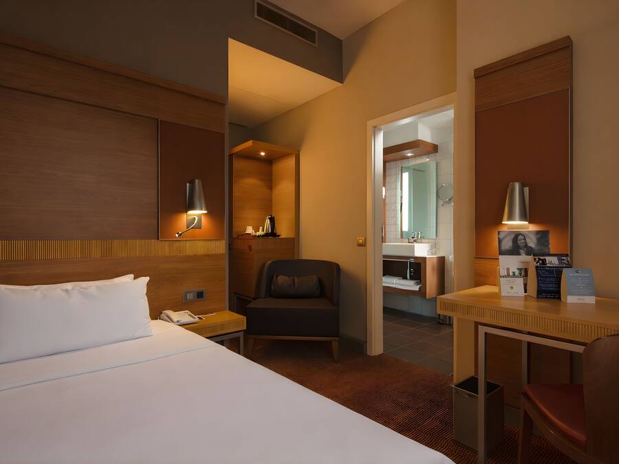 A hotel room with a bed, a desk, a chair, a bathroom, and a shower.