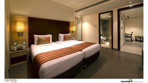 A hotel room with a large bed, bedside lamps, a nightstand, and a bathroom visible through an open door. - Cocoon Hotel (Pune)