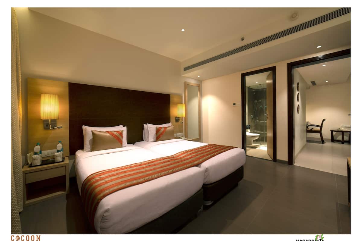 Une chambre d’hôtel avec un grand lit, des lampes de chevet, une table de nuit et une salle de bain visible à travers une porte ouverte.