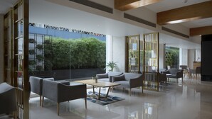 A modern hotel lobby with a glass wall, seating area, and a view of greenery outside. - Cocoon Hotel (Pune)