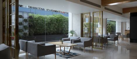 Un hall d’hôtel moderne avec un mur de verre, un espace salon et une vue sur la verdure environnante.