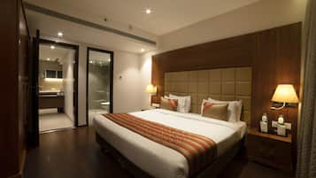A hotel room with a large bed, wooden headboard, bedside lamps, and a bathroom visible through an open door.