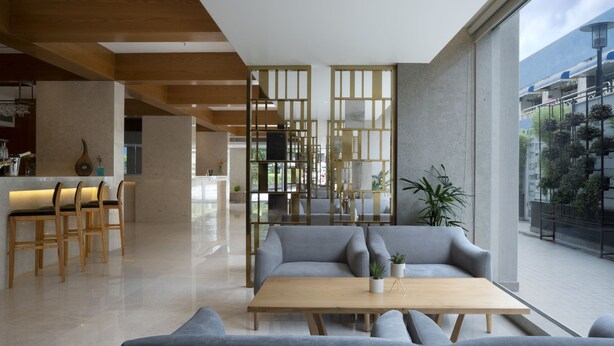 A modern interior with a sofa set, wooden tables, and a view of the city through large windows. - Cocoon Hotel (Pune)