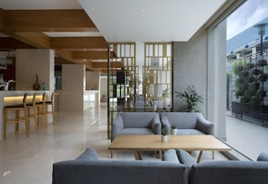 Um interior moderno com um conjunto de sofás, mesas de madeira e vista da cidade através de grandes janelas.