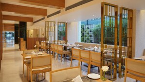 A modern dining area with wooden furniture, glass partitions, and a view of greenery outside. - Cocoon Hotel (Pune)