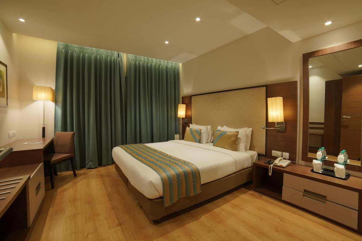 Une chambre d’hôtel avec un grand lit, un bureau, une chaise, une table de chevet avec un téléphone et un miroir.