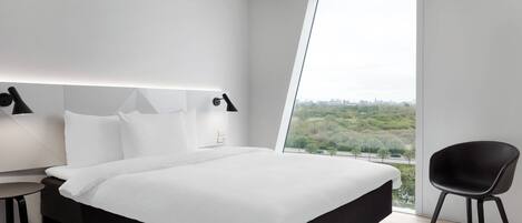 A modern hotel room with a large bed, a bedside table, a chair, and a large window offering a city view.