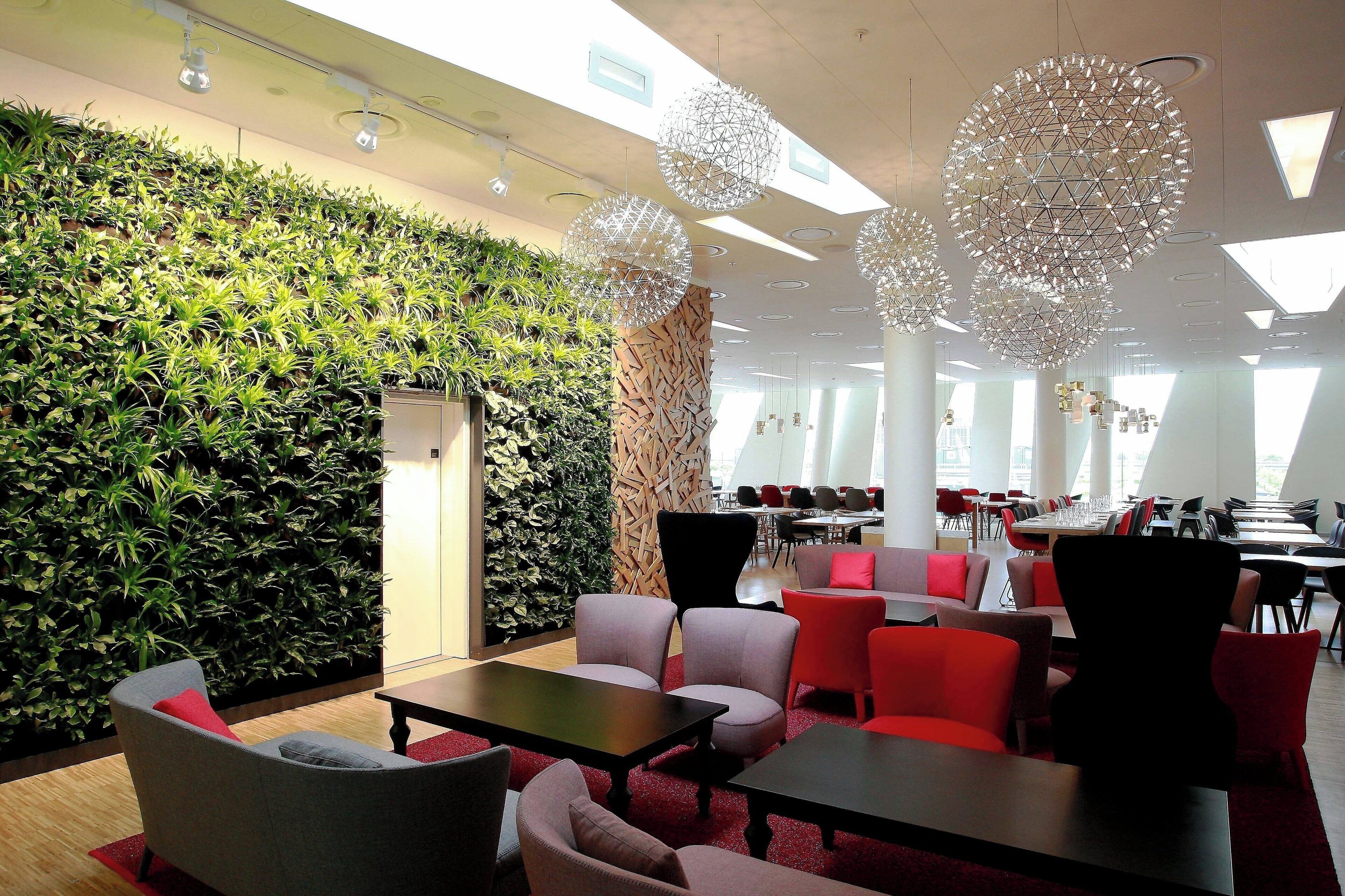 A modern lounge area with a green wall, red and grey seating, and geometric light fixtures.