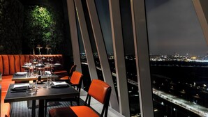 A restaurant with a city view, featuring tables and orange chairs, and a large window overlooking the cityscape. - AC Hotel by Marriott Bella Sky Copenhagen (Copenhagen)