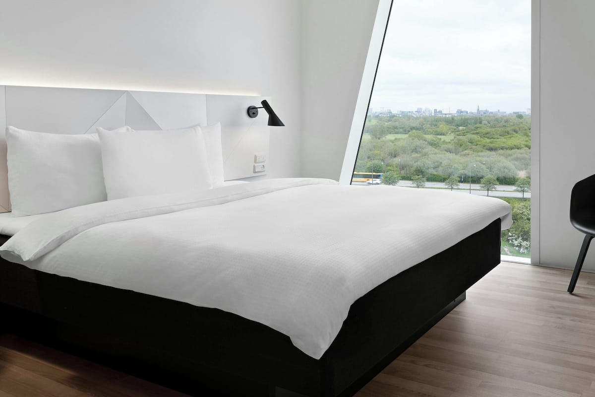 A modern hotel room with a large bed, a city view, and a minimalist design.