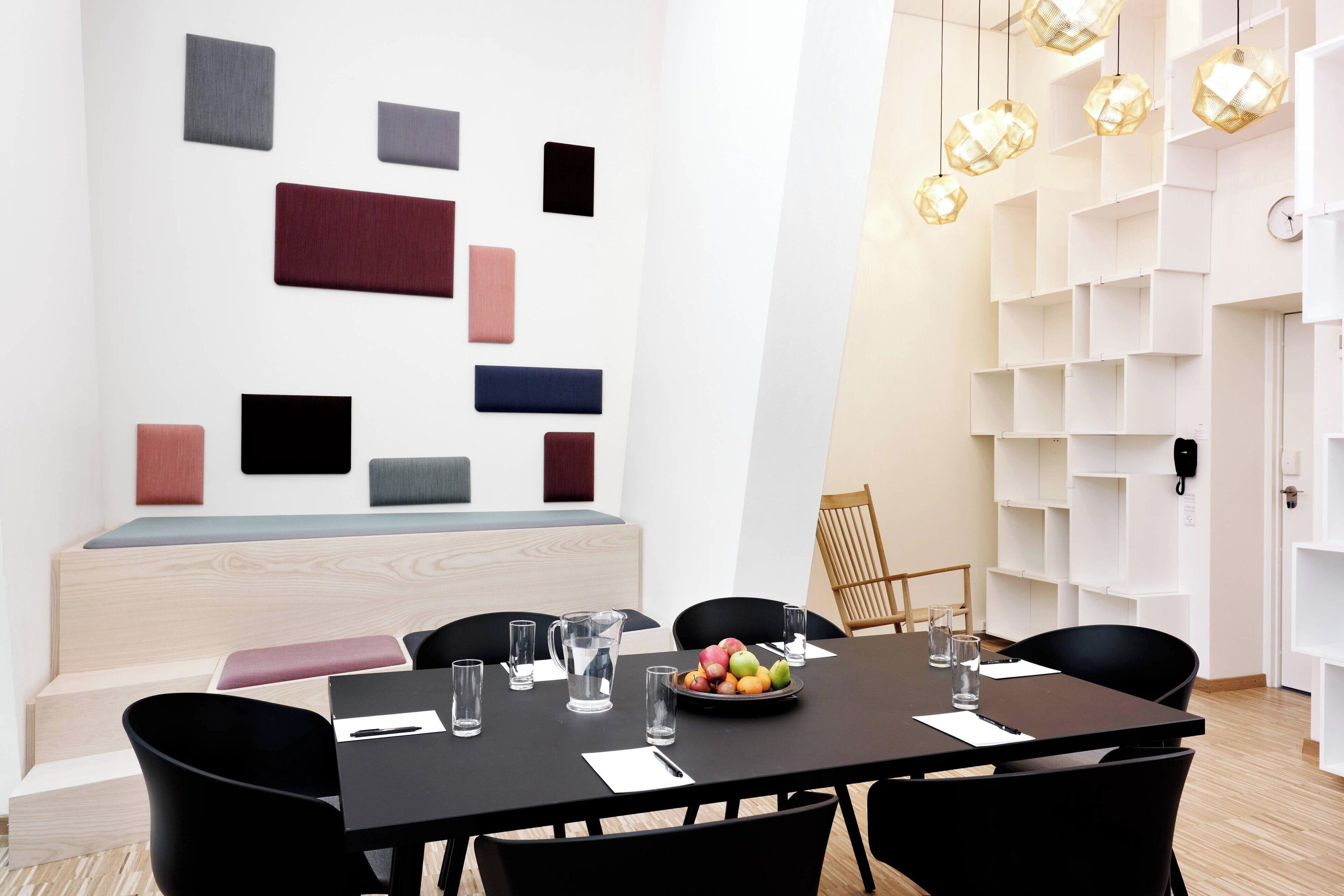 A modern dining area with a black table, black chairs, and a fruit bowl. There are white shelves with a clock and a phone on the wall.